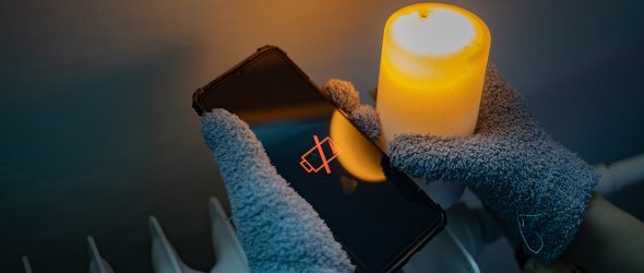 Cold Winter Blackout in Ukraine: Person in Gloves Holding Dead Phone and Candle near Cold Radiator