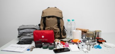 Emergency backpack equipment organized on the table. Documents, water,food, first aid kit and another items needed to survive.
