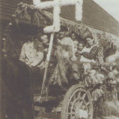 Menschen auf einem Festwagen mit einem Blumenkranz in Form eines Hakenkreuzes.