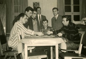 Schwarz-weiß-Bild: Eine Gruppe Männer sitzt und steht um einen Tisch herum.