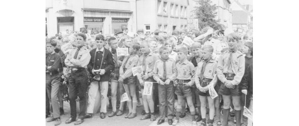 Pfadfinder auf dem Rhedaer Rathausplatz beim Wahlkampfauftritt von Bundeskanzler Ludwig Erhard. Dier Pfadfinder halten kleine Fähnchen der CDU, hinter den Pfadfindern befindet sich eine größere Menschenmenge.