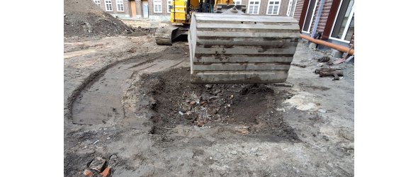 Das Bild zeigt den ehemaligen Bombentrichter mit dem Füllmaterial. Im Hintergrund ist ein Bagger und im Vordergrund eine Baggerschaufel zu sehen.