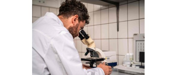 Ein Labormitarbeiter der Firma Wax Solutions im weißen Kittel schaut in ein Mikroskop.