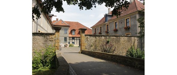 Das Bild zeigt den Gebäudekomplex von Haus Werther, wie er sich heute darstellt. Rechts das Herrenhaus von 1751, mittig das östliche Wirtschaftsgebäude, links das nördliche Wirtschaftsgebäude. Blick vom „Jägerhaus“ aus über die steinerne Brücke und das Tor auf den Innenhof.