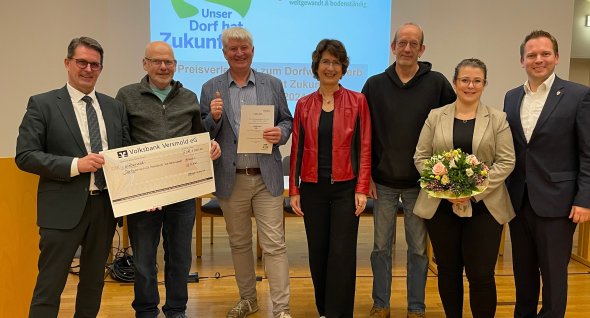 Personen stehen nebeneinander, einige halten etwas in den Händen (z.B. einen Blumenstrauß).