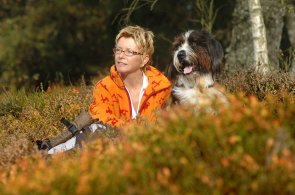 Frau mit Hund sitzt in der Heide und macht Pause vom Wandern