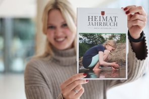 Junge Frau hält das Cover des Heimatjahrbuchs 2022 in die Kamera Junge Frau hält das Cover des Heimatjahrbuchs 2022 in die Kamera